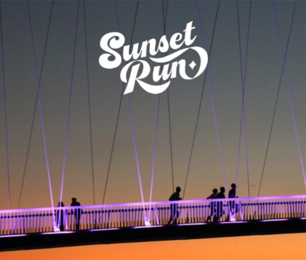 Trkači prelaze pješački most u Osijeku tijekom večernje utrke Sunset Run u vrijeme zalaska sunca.