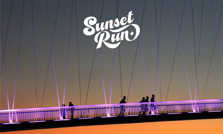 Trkači prelaze pješački most u Osijeku tijekom večernje utrke Sunset Run u vrijeme zalaska sunca.